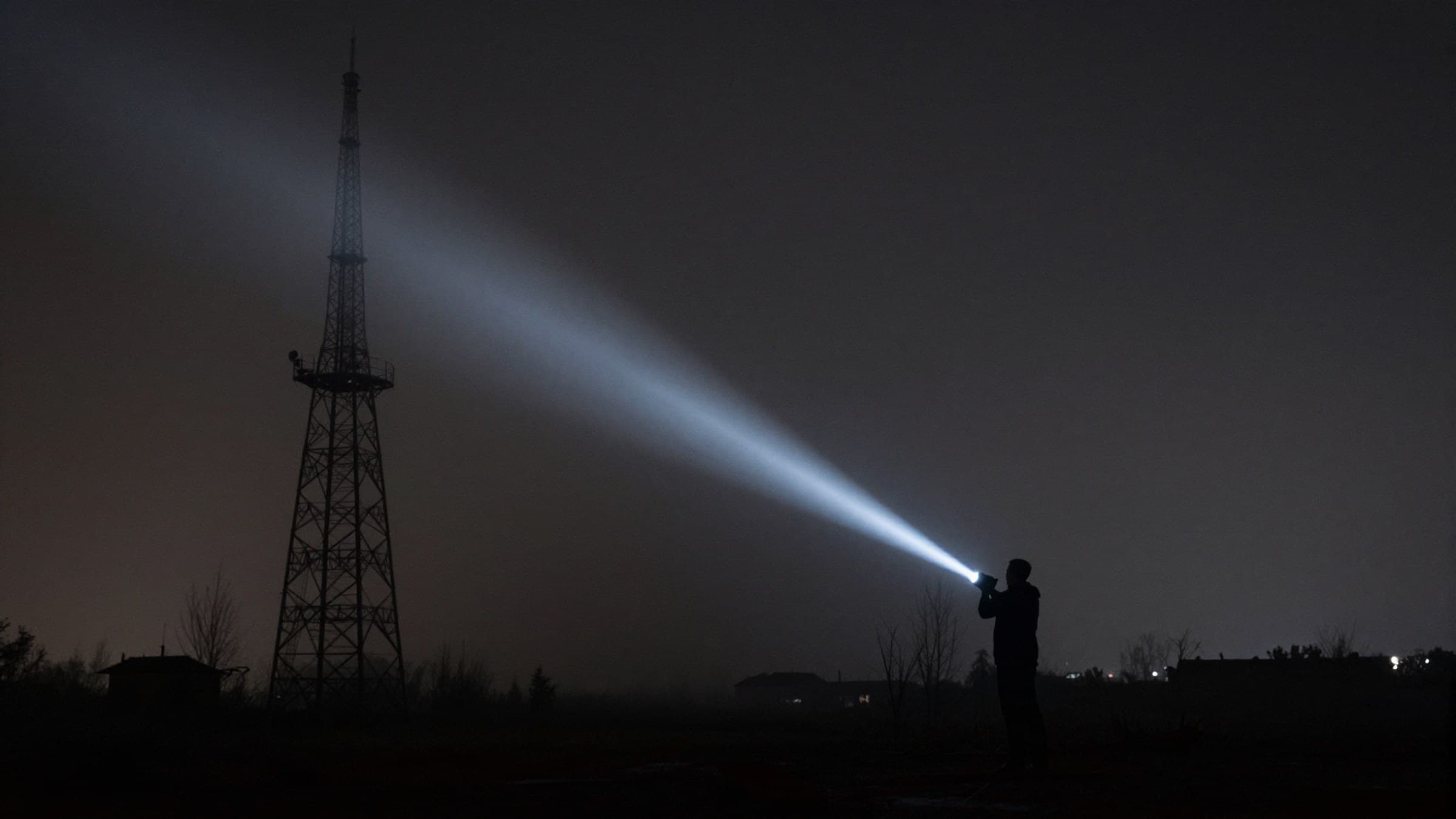 A lone flashlight beam cutting through fog near an abandoned radio tower at night, cinematic and moody